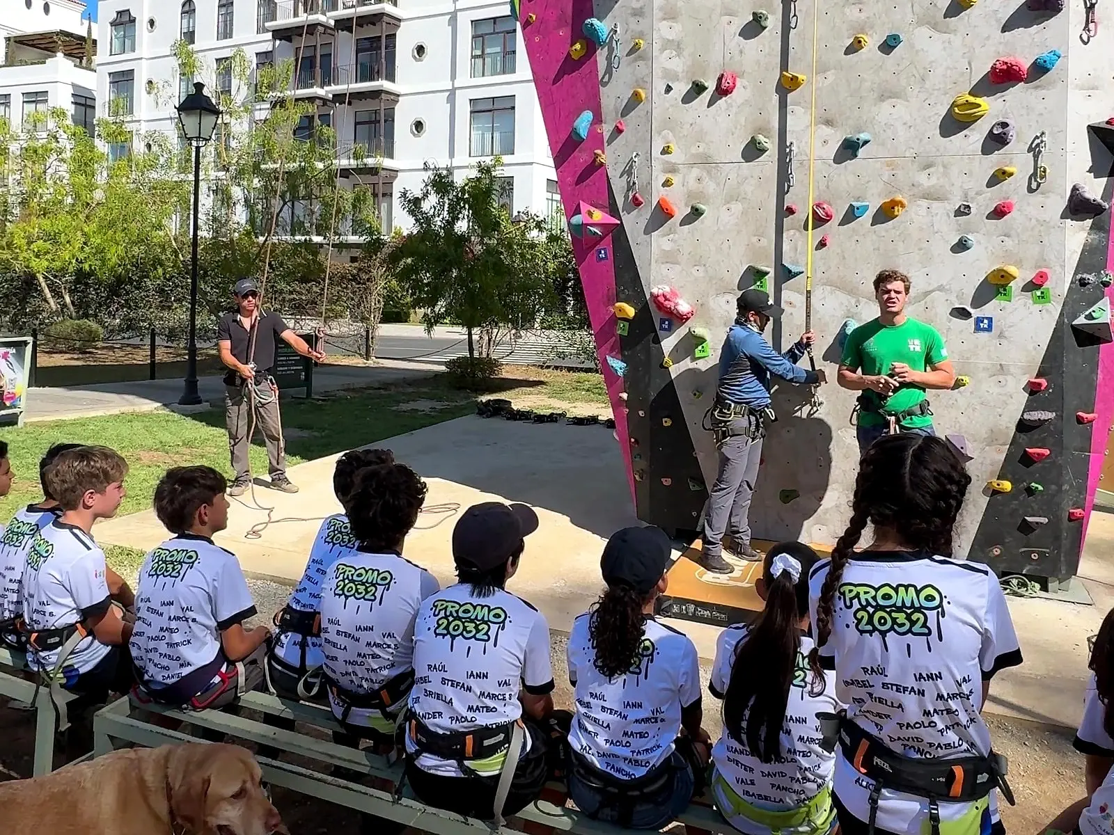 Alumnos de excursión con arneses, sentados al pie de El Muro, escuchando a los instructores antes de escalar