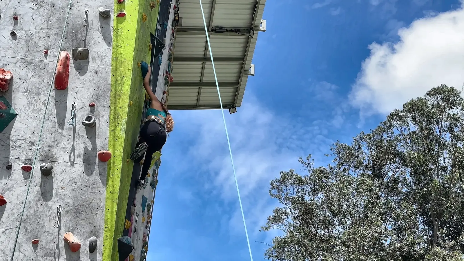 Escaladora en la pared verde de El Muro, con el cielo azul detrás